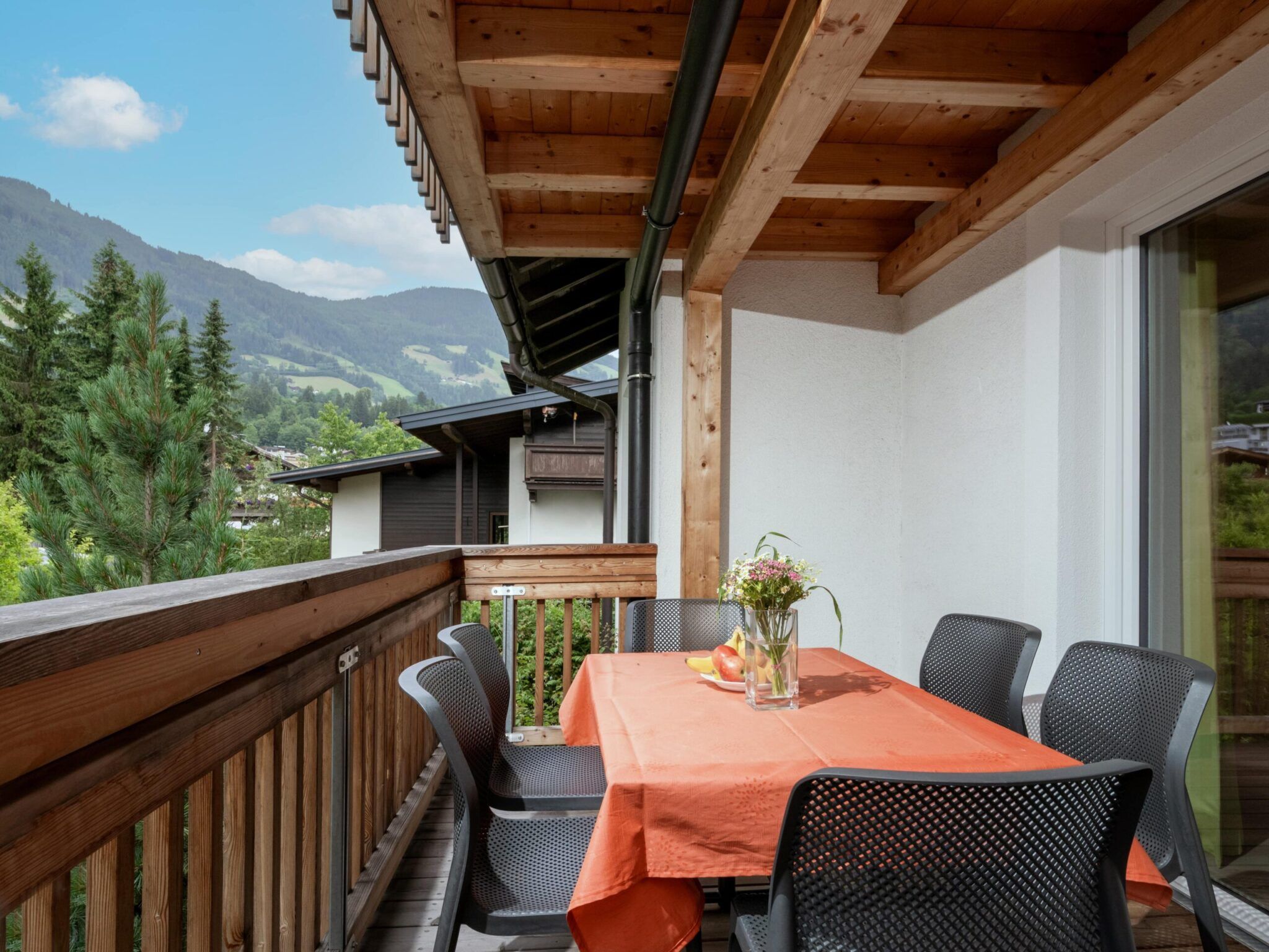 Ein Balkon mit einem Holztisch, einer Blumenvase und Stühlen und Blick auf eine malerische Berglandschaft.