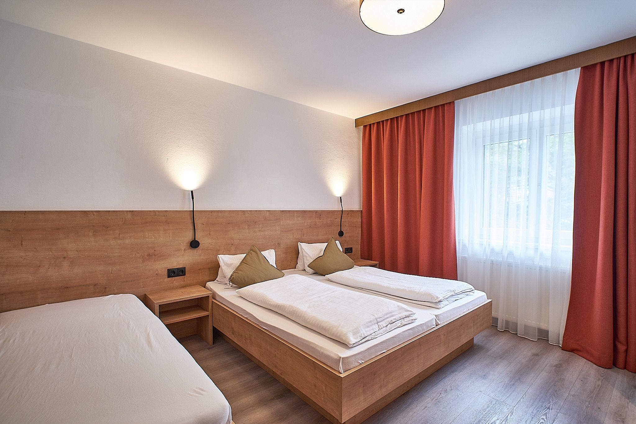 Ein ordentliches Hotelzimmer mit zwei Betten, Holzakzenten, roten Vorhängen und sanfter Beleuchtung.