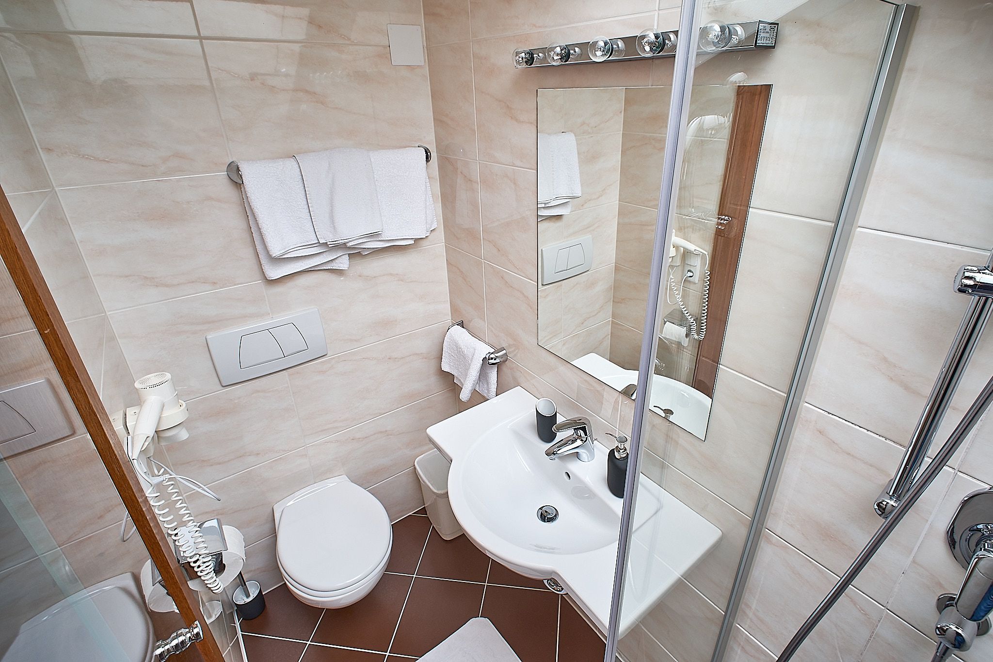 Kleines Badezimmer mit Dusche, Waschbecken und Toilette. Handtücher hängen an einem Ständer und über dem Waschbecken befindet sich ein Spiegel.