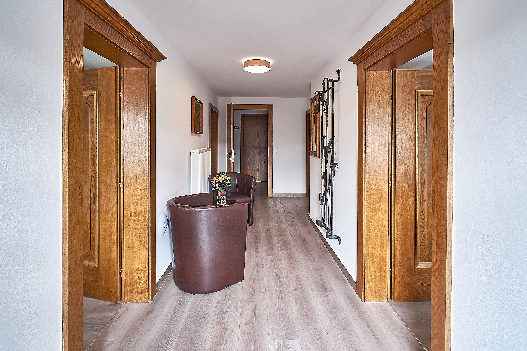 Flur mit Holztüren, braunen Stühlen und einem kleinen Tisch mit Blumen auf einem Holzboden.