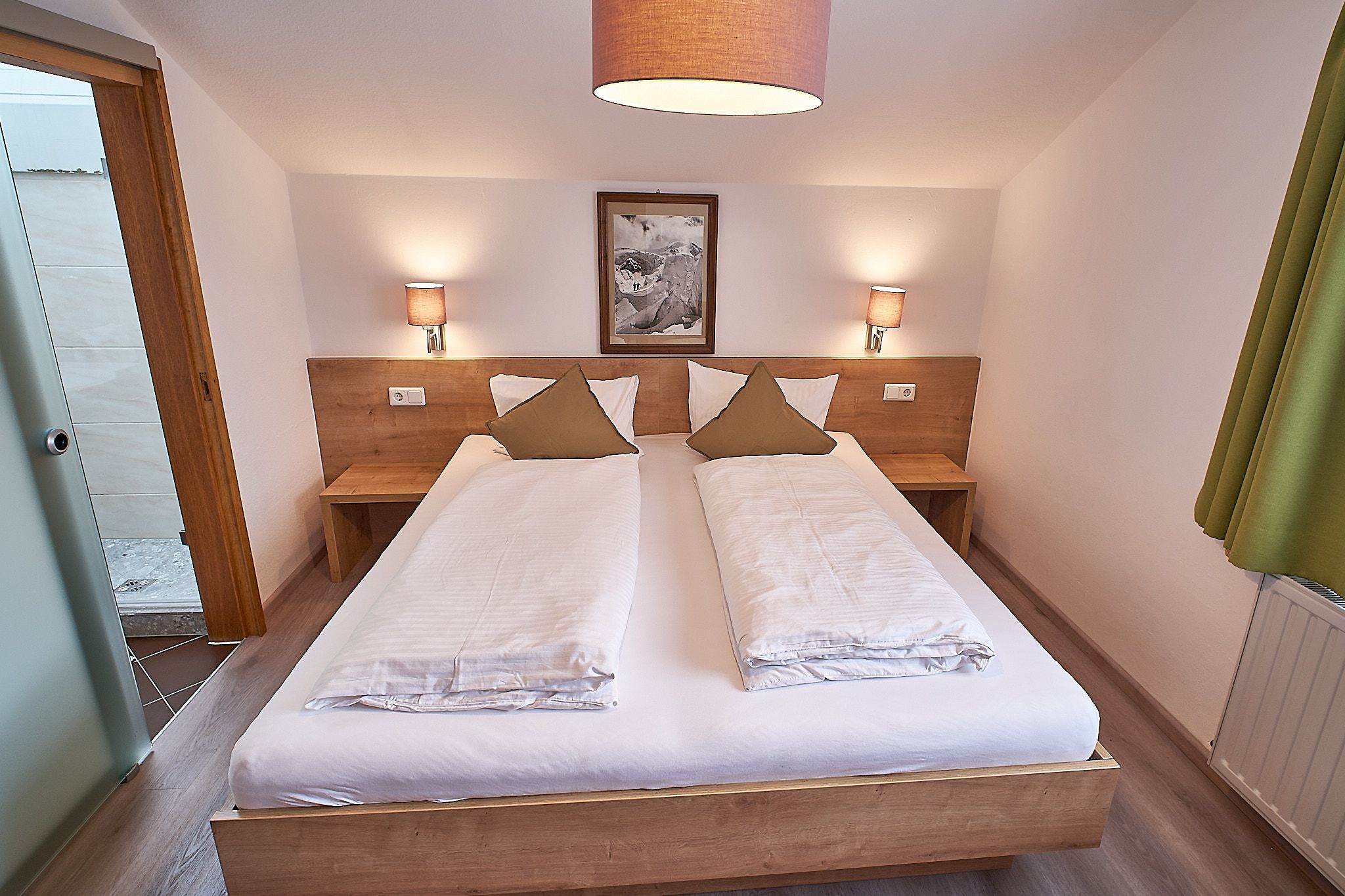 Gemütliches Schlafzimmer mit einem Doppelbett aus Holz, weißer Bettwäsche, zwei Wandlampen und einem gerahmten Bild über dem Kopfteil.
