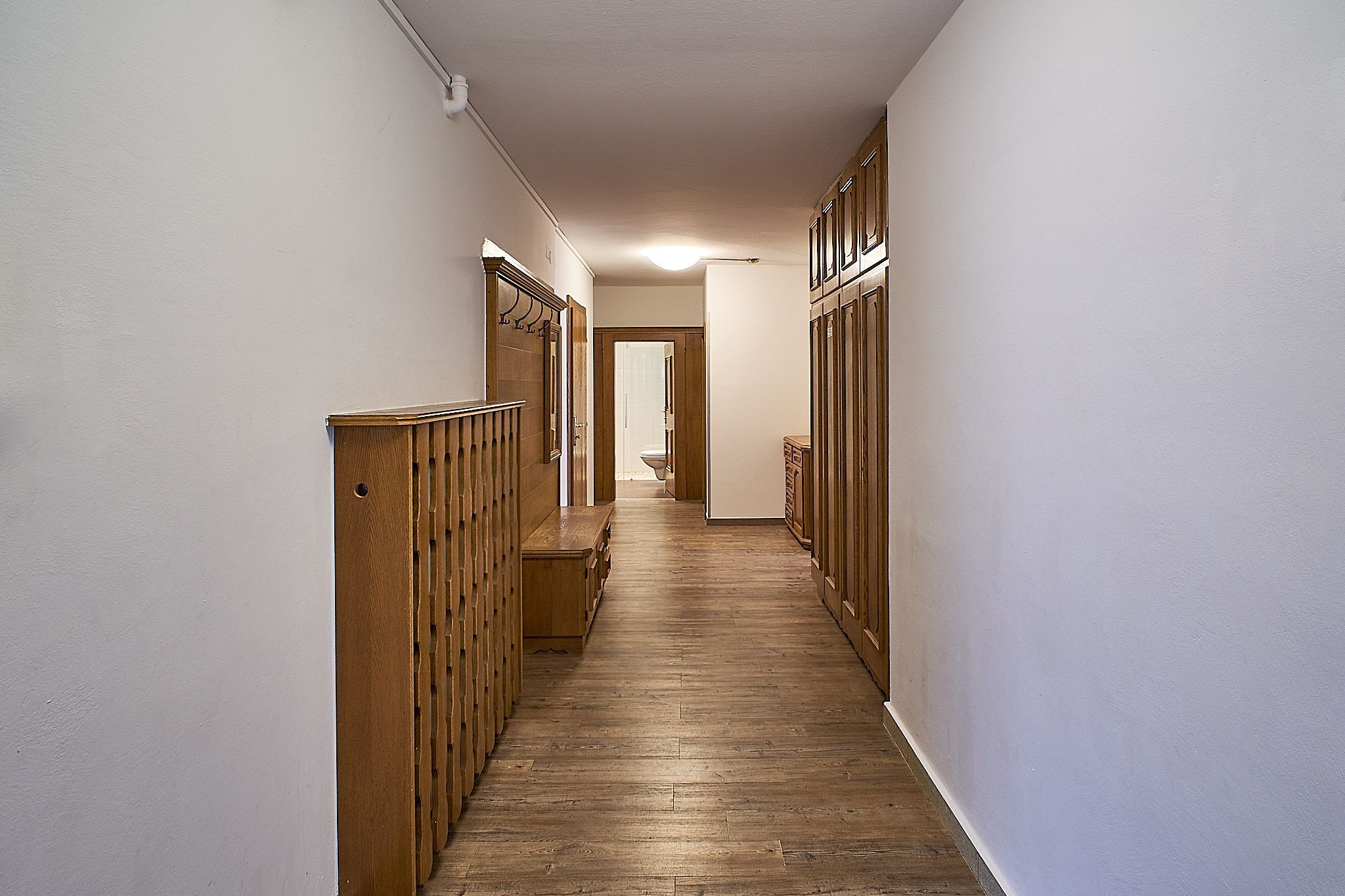 Ein langer Flur mit Holzböden, Holzvertäfelung und einer Tür, die am Ende zu einem Badezimmer führt.